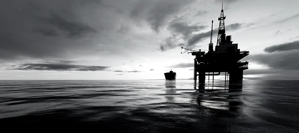 An offshore oil platform and a tanker ship silhouetted on the sea at dusk